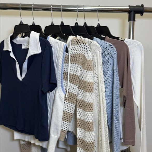 A display of eight different tops hanging on a rack, featuring various colors and styles including a navy blue polo with a white collar, a white knit sweater, and a brown long-sleeve shirt among others.