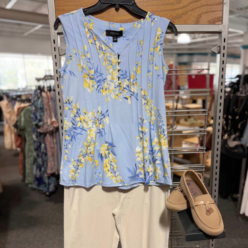 Image of blue tanktop with white flowers hanging on a rack with cream pants and tan loafers