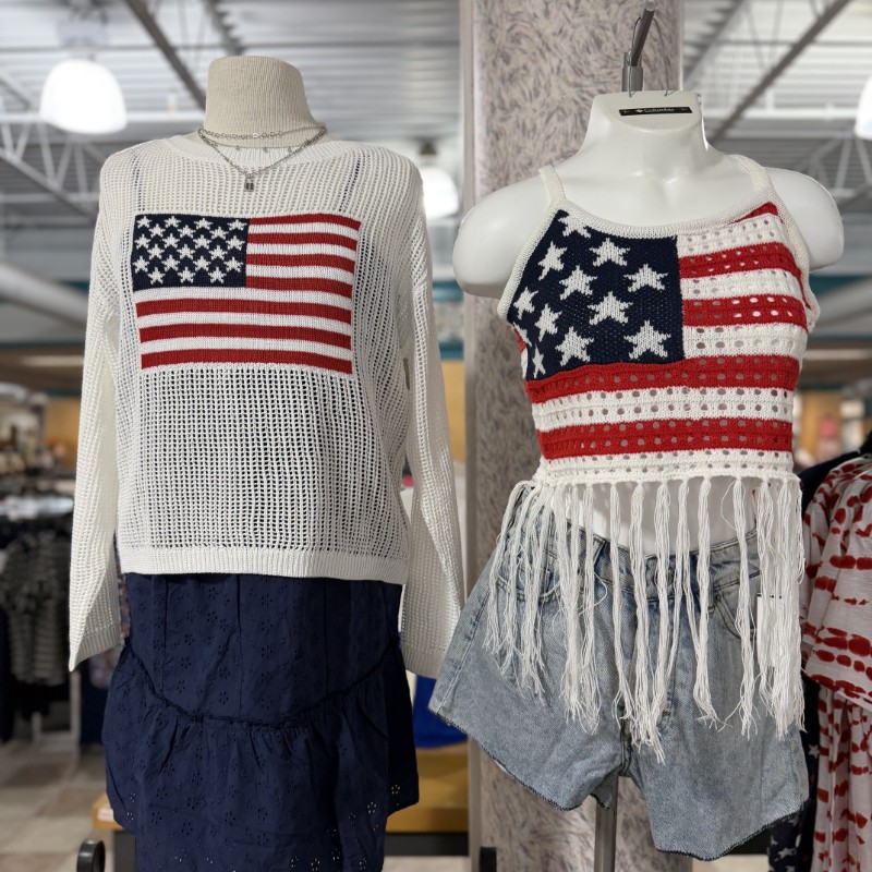 White American flag sweater on a manikin with a blue skirt next to another manikin wearing an American flag tank top and denim shorts.